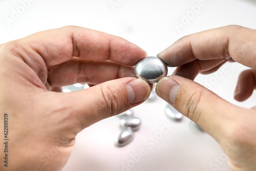 Man's hand holding a lump of silver or platinum or a rare earth mineral on white background