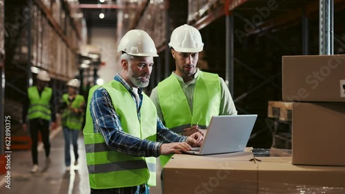 Two Workers Using Laptop in Logistic Centre, to Checking the Orders Before Deliveries. Boss Showing to Engineer New Work Plan on the Computer