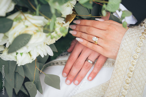 Close Up of Bride and Groom Holding Hands with Wedding Rings and White Flowers – Muslim Wedding, Marriage Ceremony, Love, Romance, Commitment, Engagement, Bridal Jewelry, Islamic Culture, Marriage