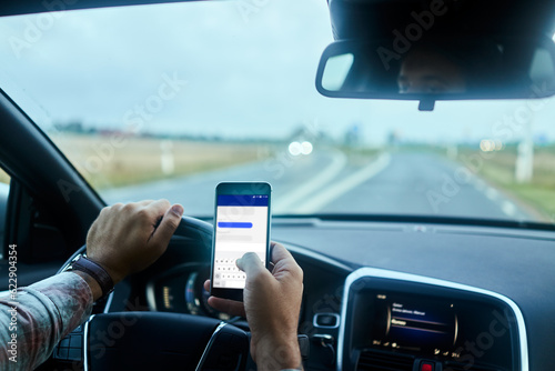 Man using a smart phone while driving a car on the road