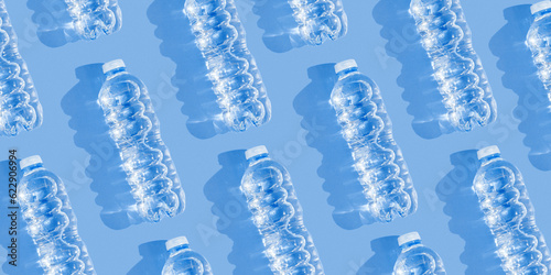 Pattern small plastic bottles with clean drinking water at sunlight, shadow on blue background, banner. Full closed bottle water. Pollution, plastic garbage, non-biodegradable packaging waste
