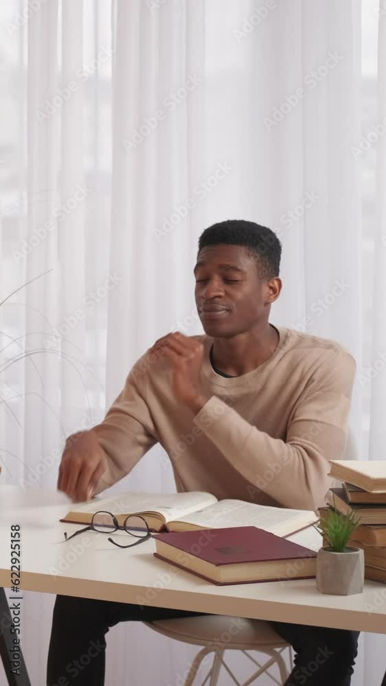 Vertical video. Education stress. Hard exam. Difficult study. Exhausted man with eyestrain neck pain reading book preparing homework research at home desk copy space. Vertical video. Education stress. Hard exam. Difficult study. Exhausted man with eyestrain neck pain reading book preparing homework research at home desk copy space.