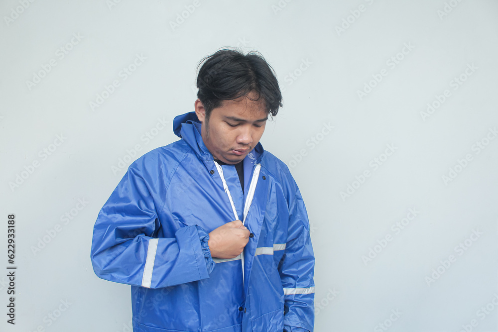 Young Asian man wearing blue raincoat on gray background. Young Asian man wearing blue raincoat on gray background.