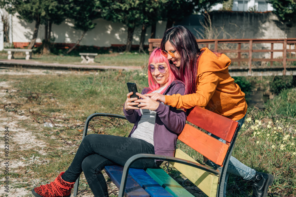 couple of homosexual girls with mobile phone on park bench lgtbi couple of homosexual girls with mobile phone on park bench lgtbi