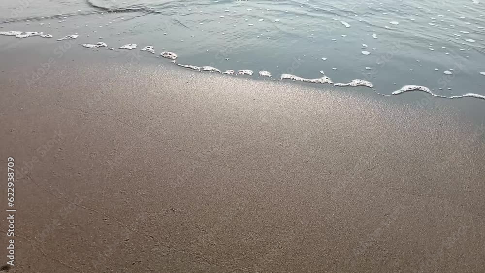 Waves crashing on the beach, flowing over grains of sand Waves crashing on the beach, flowing over grains of sand
