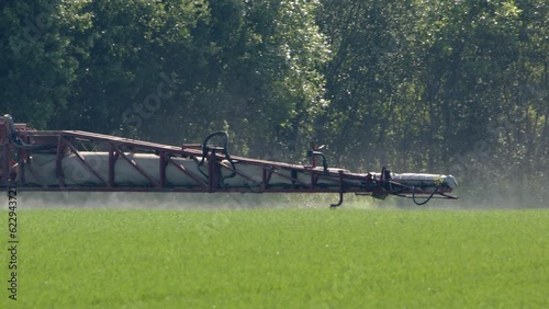 Crops on farm land being sprayed by boom arm of sprayer tractor, tele shot photo