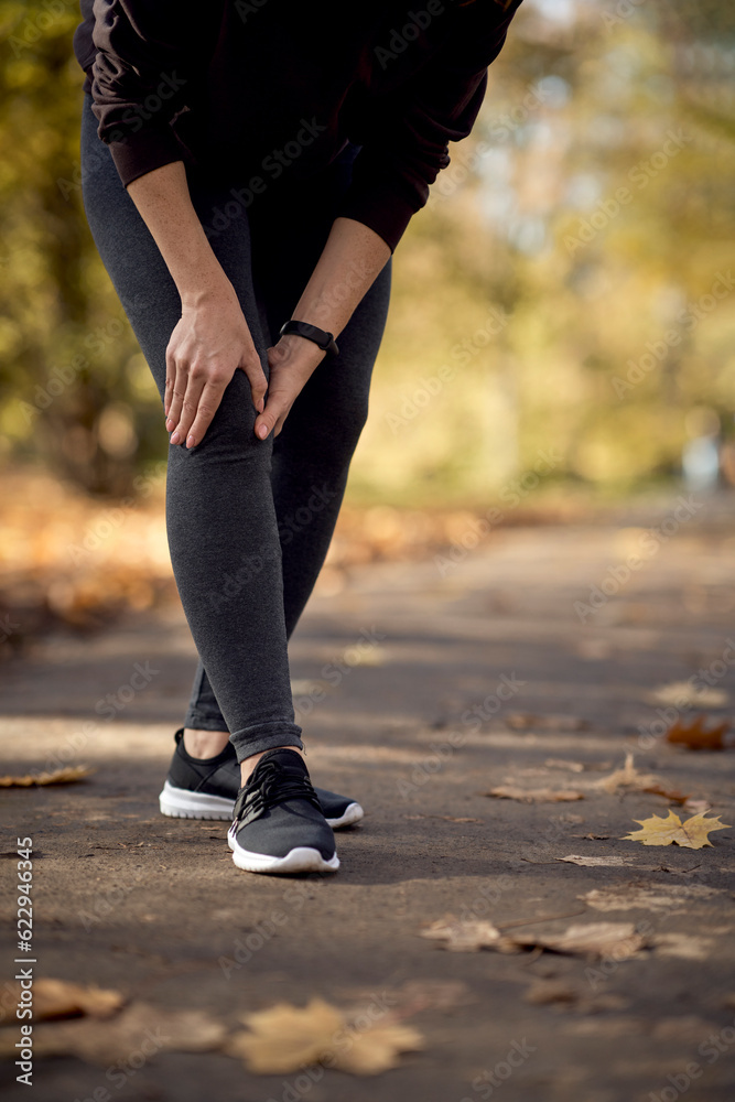 Low section of woman feeling knee injury during jogging in the park