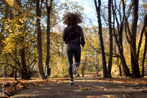 Rear view of caucasian woman jogging in the park in the autumn
