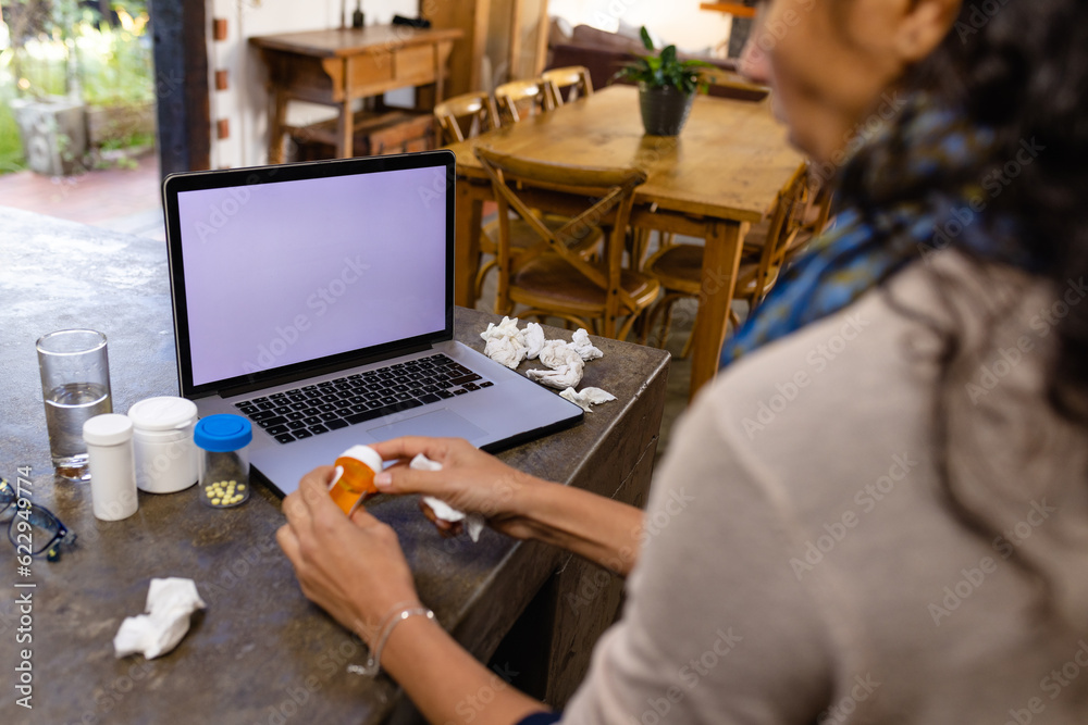 Biracial woman sitting at countertop, using laptop with copy space for medical consultation