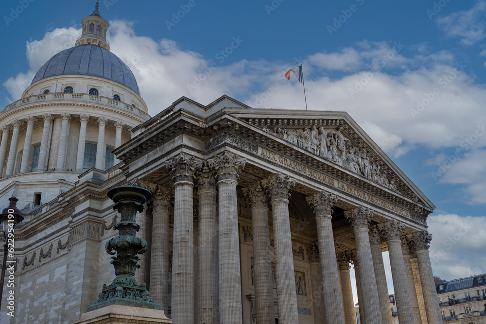 Pantheon building in Paris, France with focus on French flag over blue sky.