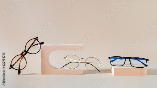Glasses sale banner. Optic store sale-out offer. Trendy glasses in plastic and metallic frame on podiums on beige background. Eyewear collection. Copy space for text. Optic store discount. Minimalism photo