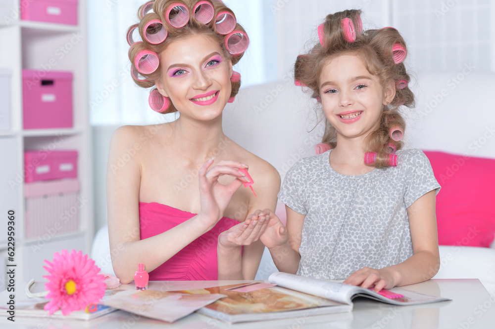 Mom and daughter with hair curlers reading magazine Mom and daughter with hair curlers reading magazine