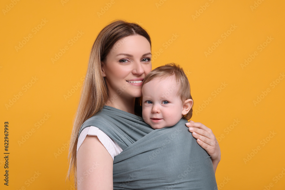Mother holding her child in baby wrap on orange background Mother holding her child in baby wrap on orange background
