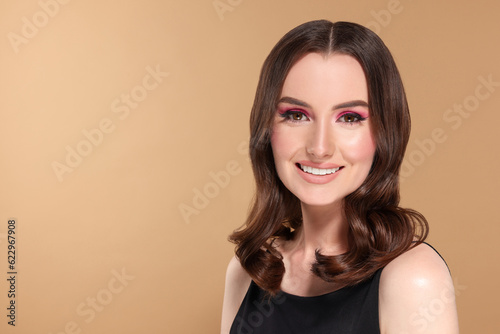 Portrait of beautiful young woman with makeup and gorgeous hair styling on beige background. Space for text