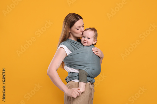 Mother holding her child in baby wrap on orange background © New Africa