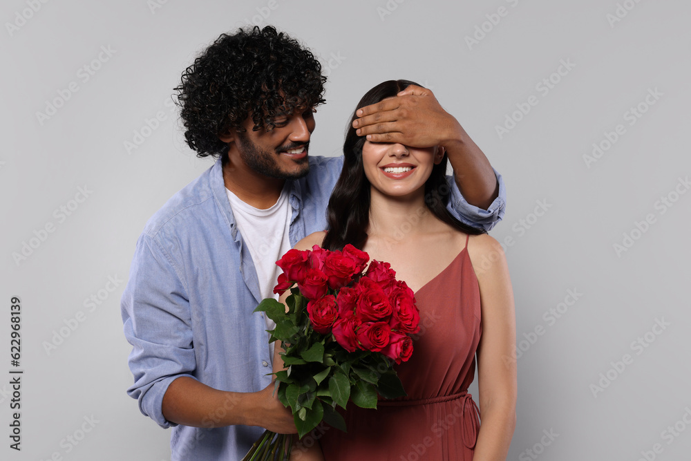 International dating. Handsome man presenting roses to his beloved woman on light grey background