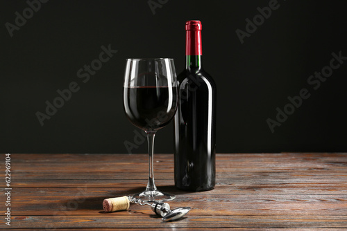 Corkscrew, glass and bottle of red wine on wooden table against black background © New Africa
