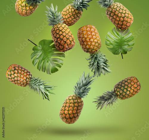 Fresh pineapples and monstera leaves falling on green background