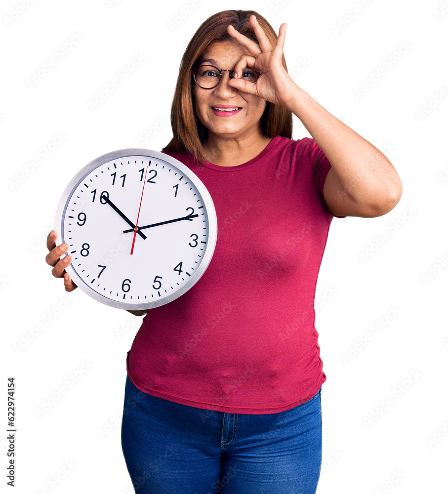 Middle age latin woman holding big clock smiling happy doing ok sign with hand on eye looking through fingers Middle age latin woman holding big clock smiling happy doing ok sign with hand on eye looking through fingers