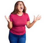 Middle age latin woman wearing casual clothes and glasses crazy and mad shouting and yelling with aggressive expression and arms raised. frustration concept.