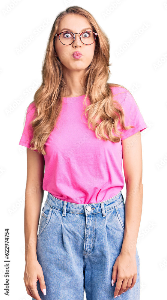 Obraz premium Young beautiful caucasian woman with blond hair wearing casual clothes and glasses puffing cheeks with funny face. mouth inflated with air, crazy expression.