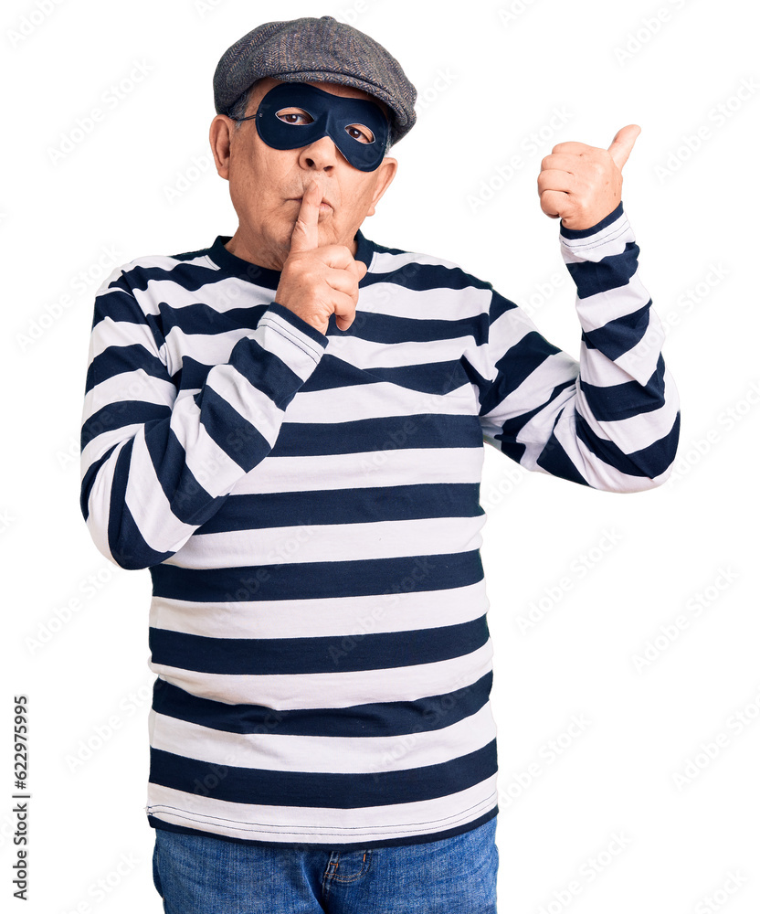 Senior handsome man wearing burglar mask and t-shirt asking to be quiet with finger on lips pointing with hand to the side. silence and secret concept. Senior handsome man wearing burglar mask and t-shirt asking to be quiet with finger on lips pointing with hand to the side. silence and secret concept.