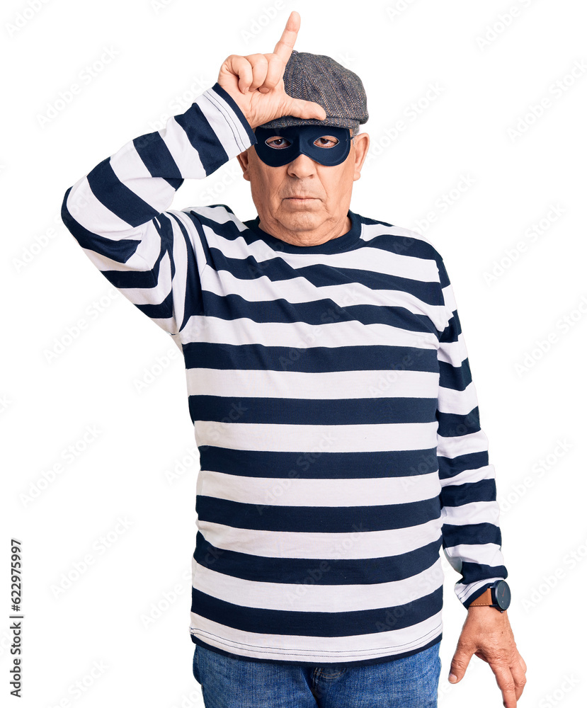 Senior handsome man wearing burglar mask and t-shirt making fun of people with fingers on forehead doing loser gesture mocking and insulting. Senior handsome man wearing burglar mask and t-shirt making fun of people with fingers on forehead doing loser gesture mocking and insulting.