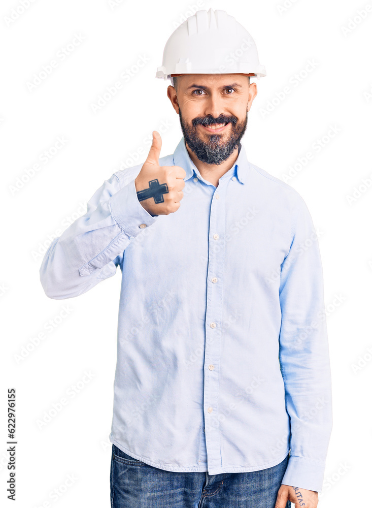 Young handsome man wearing architect hardhat doing happy thumbs up gesture with hand. approving expression looking at the camera showing success. Young handsome man wearing architect hardhat doing happy thumbs up gesture with hand. approving expression looking at the camera showing success.