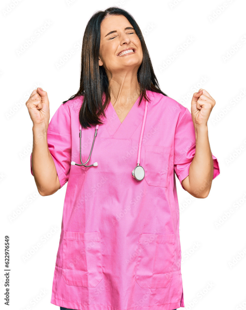 Middle age brunette woman wearing doctor uniform and stethoscope very happy and excited doing winner gesture with arms raised, smiling and screaming for success. celebration concept. Middle age brunette woman wearing doctor uniform and stethoscope very happy and excited doing winner gesture with arms raised, smiling and screaming for success. celebration concept.