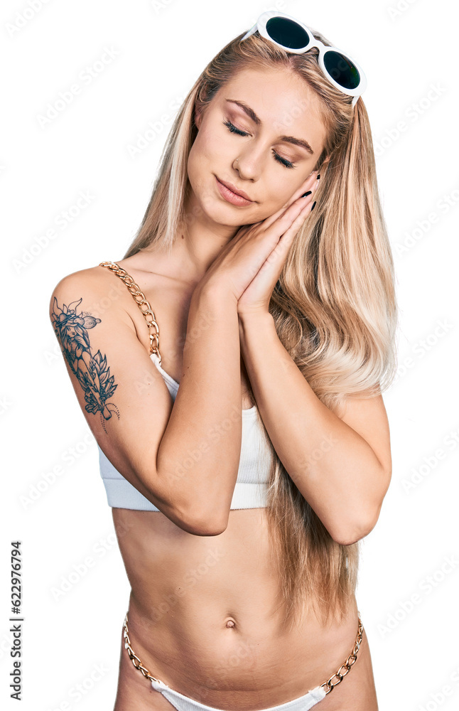Naklejka premium Beautiful young blonde woman wearing bikini sleeping tired dreaming and posing with hands together while smiling with closed eyes.