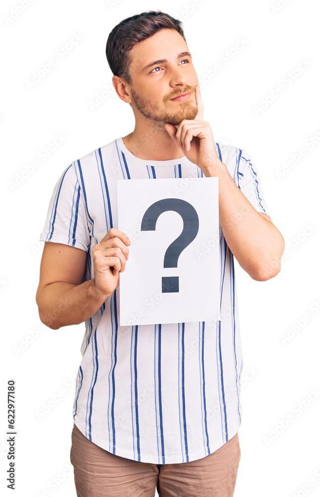 Handsome young man with bear holding question mark serious face thinking about question with hand on chin, thoughtful about confusing idea Handsome young man with bear holding question mark serious face thinking about question with hand on chin, thoughtful about confusing idea