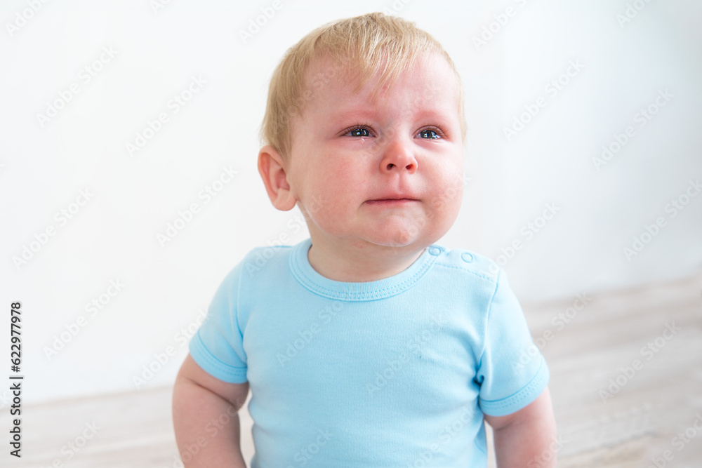 blonde baby in blue shirt crying sitting on floor at home blonde baby in blue shirt crying sitting on floor at home