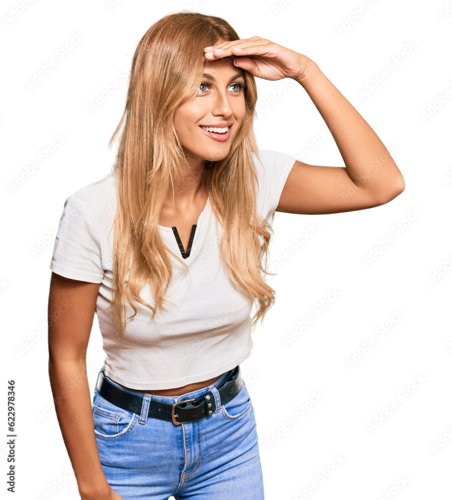 Beautiful blonde young woman wearing casual white tshirt very happy and smiling looking far away with hand over head. searching concept. Beautiful blonde young woman wearing casual white tshirt very happy and smiling looking far away with hand over head. searching concept.