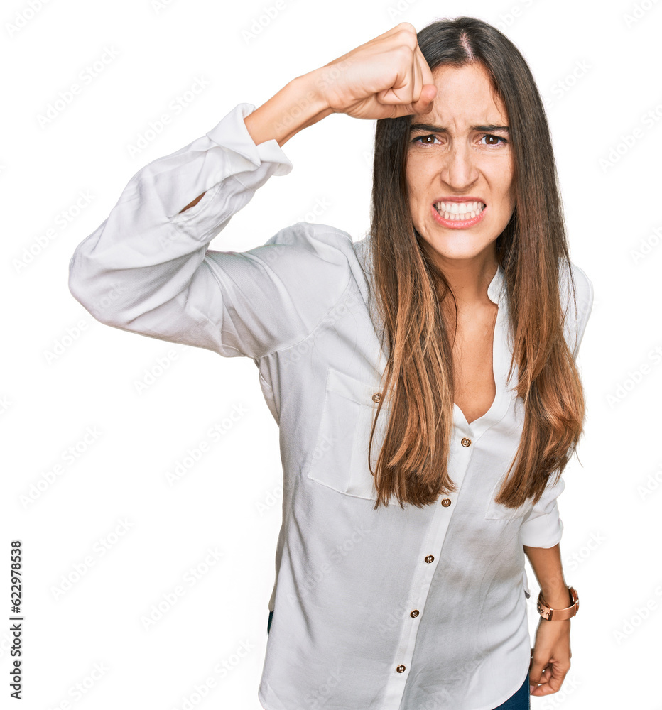 Young beautiful woman wearing casual clothes angry and mad raising fist frustrated and furious while shouting with anger. rage and aggressive concept. Young beautiful woman wearing casual clothes angry and mad raising fist frustrated and furious while shouting with anger. rage and aggressive concept.