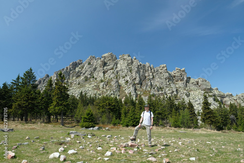 The guy, a tourist, stands tall against the background of a rock. Summer, day, blue sky.
