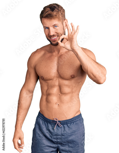 Young caucasian man standing shirtless smiling positive doing ok sign with hand and fingers. successful expression.