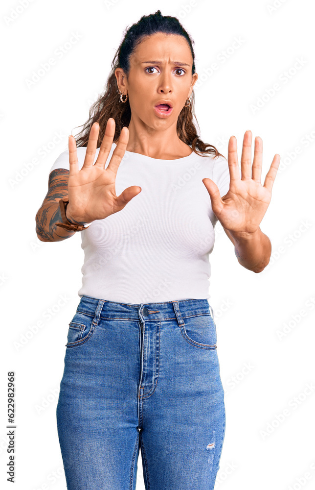 Young hispanic woman with tattoo wearing casual white tshirt doing stop gesture with hands palms, angry and frustration expression Young hispanic woman with tattoo wearing casual white tshirt doing stop gesture with hands palms, angry and frustration expression
