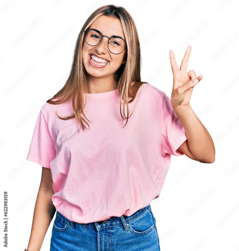 Hispanic young woman wearing casual t shirt and glasses smiling with happy face winking at the camera doing victory sign. number two. Hispanic young woman wearing casual t shirt and glasses smiling with happy face winking at the camera doing victory sign. number two.