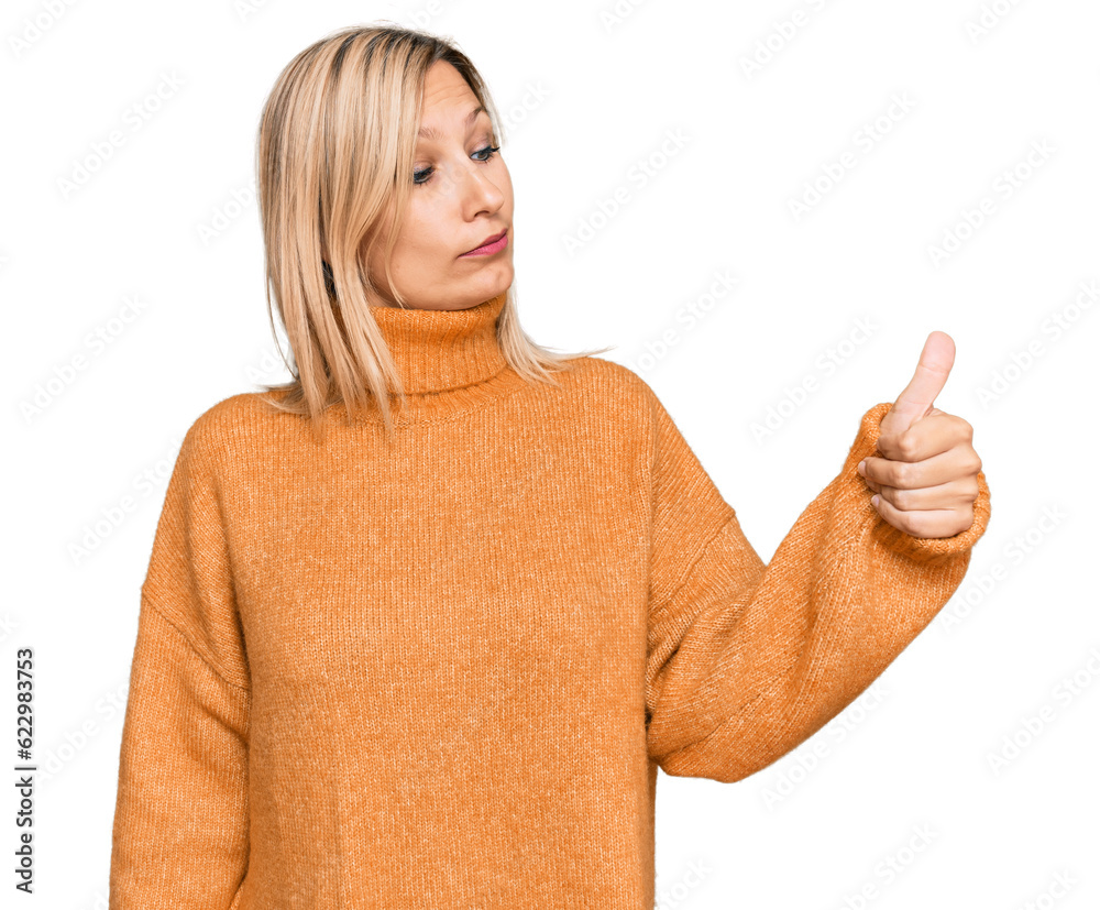 Middle age caucasian woman wearing casual winter sweater looking proud, smiling doing thumbs up gesture to the side