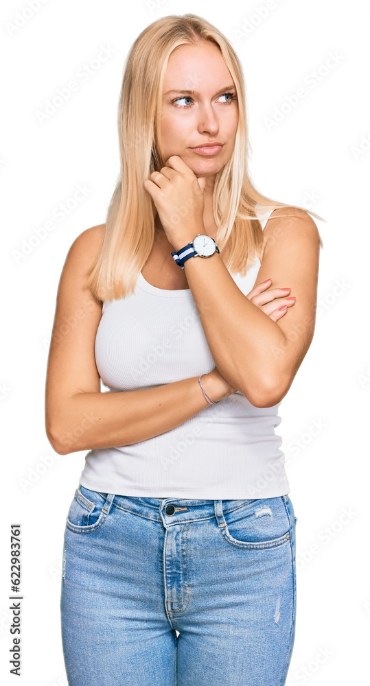 Young blonde girl wearing casual style with sleeveless shirt with hand on chin thinking about question, pensive expression. smiling with thoughtful face. doubt concept. Young blonde girl wearing casual style with sleeveless shirt with hand on chin thinking about question, pensive expression. smiling with thoughtful face. doubt concept.