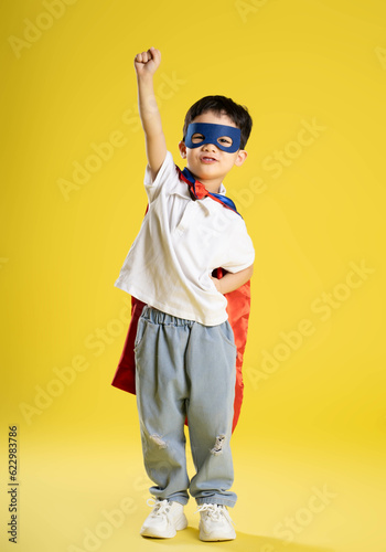 Fototapeta full body image of a boy wearing a superhero shirt posing on a yellow background
