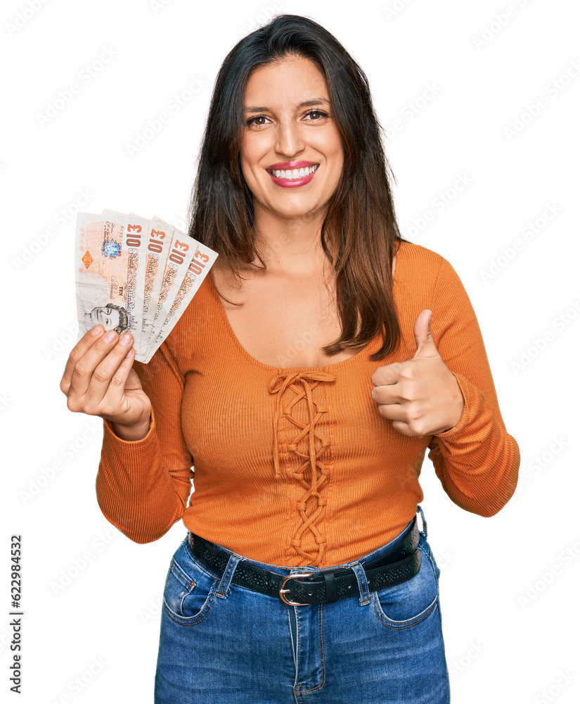 Beautiful hispanic woman holding 10 united kingdom pounds banknotes smiling happy and positive, thumb up doing excellent and approval sign Beautiful hispanic woman holding 10 united kingdom pounds banknotes smiling happy and positive, thumb up doing excellent and approval sign