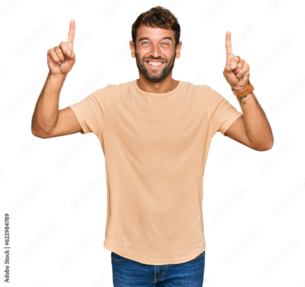 Handsome young man with beard wearing casual tshirt smiling amazed and surprised and pointing up with fingers and raised arms. Handsome young man with beard wearing casual tshirt smiling amazed and surprised and pointing up with fingers and raised arms.