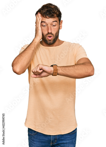 Handsome young man with beard wearing casual tshirt looking at the watch time worried, afraid of getting late