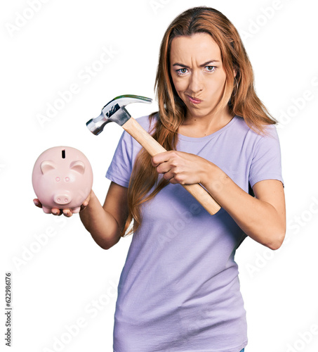 Young caucasian woman holding piggy bank and hammer skeptic and nervous  frowning upset because of problem. negative person.