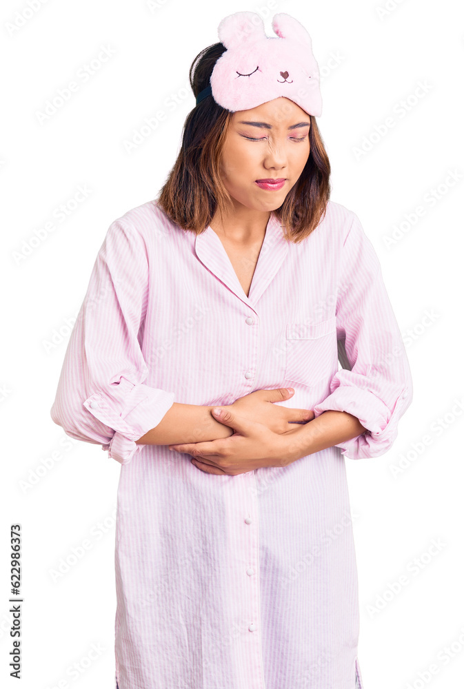 Young beautiful chinese girl wearing sleep mask and pajama with hand on stomach because indigestion, painful illness feeling unwell. ache concept. Young beautiful chinese girl wearing sleep mask and pajama with hand on stomach because indigestion, painful illness feeling unwell. ache concept.