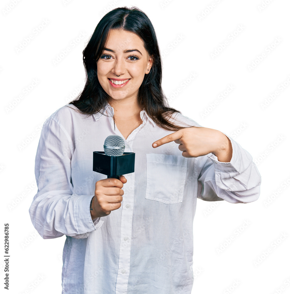 Beautiful hispanic woman holding reporter microphone smiling happy pointing with hand and finger Beautiful hispanic woman holding reporter microphone smiling happy pointing with hand and finger