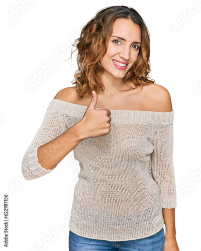 Beautiful young caucasian woman wearing casual clothes doing happy thumbs up gesture with hand. approving expression looking at the camera showing success.