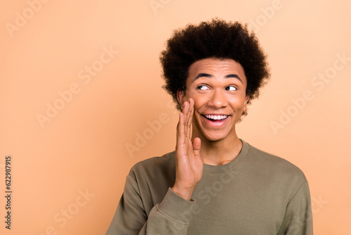Portrait of nice cheerful person afro hairdo dressed khaki pullover look empty space telling rumors isolated on beige color background © deagreez