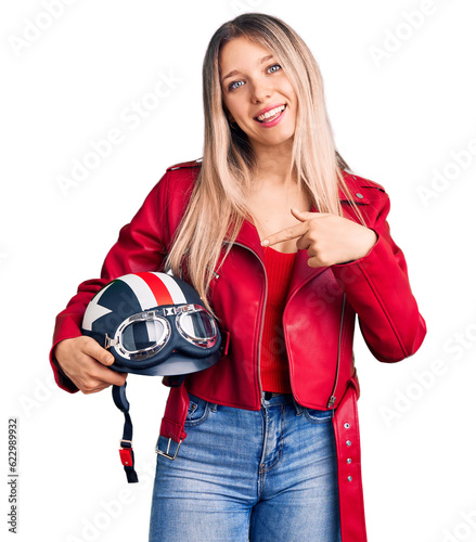 Young beautiful blonde woman holding motorcycle helmet smiling happy pointing with hand and finger